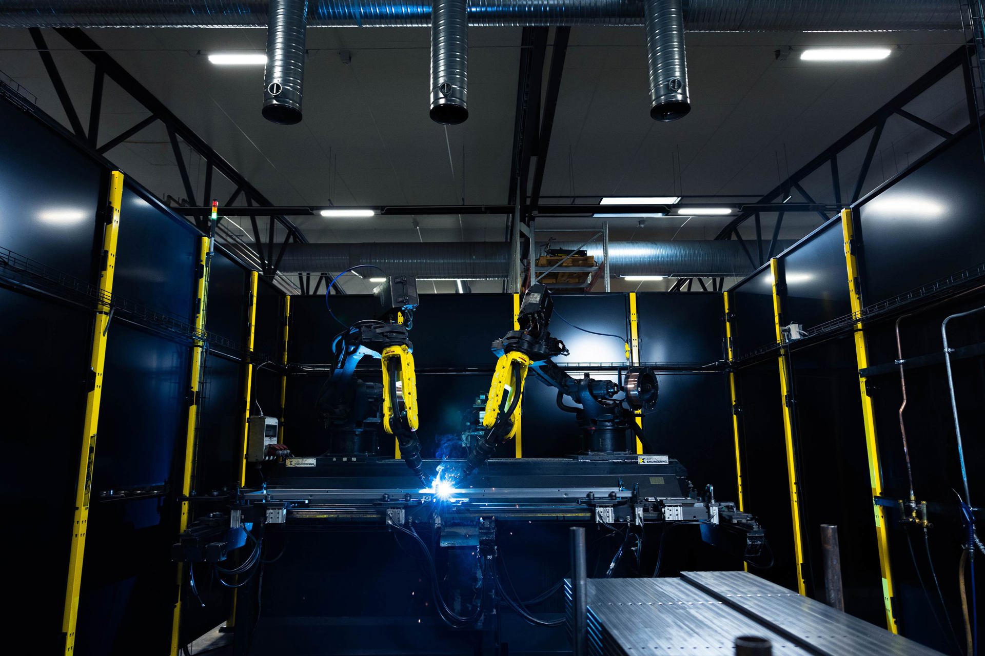 Koruma panelleri arkasında kaynak işlemi yapan iki endüstriyel robot